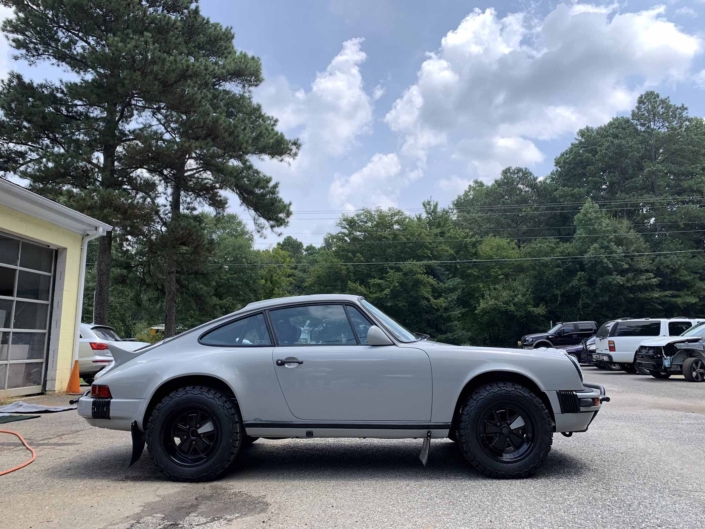 side view of a rear view of a custom 1986 Porsche 911 Carrera with Chalk exterior color and Porsche Pepita interior parked in front of a garage