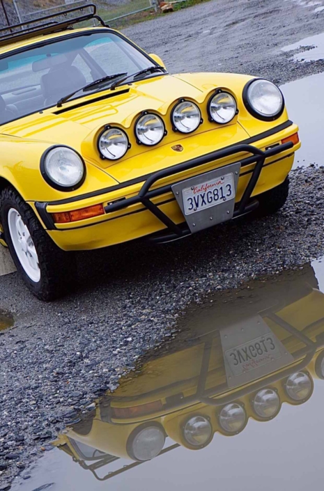 headlight shot of a Custom Built 1988 Porsche 911 Carrera with Cadmium Yellow exterior and Opel fabric interior parked in front of a puddle