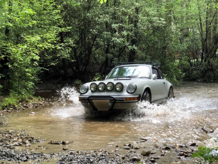 Custom Built 1986 Porsche 911 Carrera with Fashion Grey Exterior and Lancia Fabric Interior driving through the water in the woods