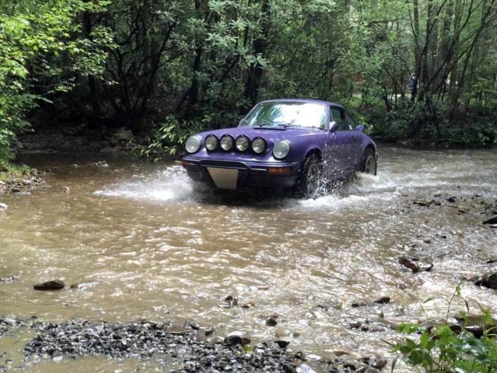 Custom Built 1978 Porsche 911 SC with Lilac exterior and Pascha interio driving through the water in the woods