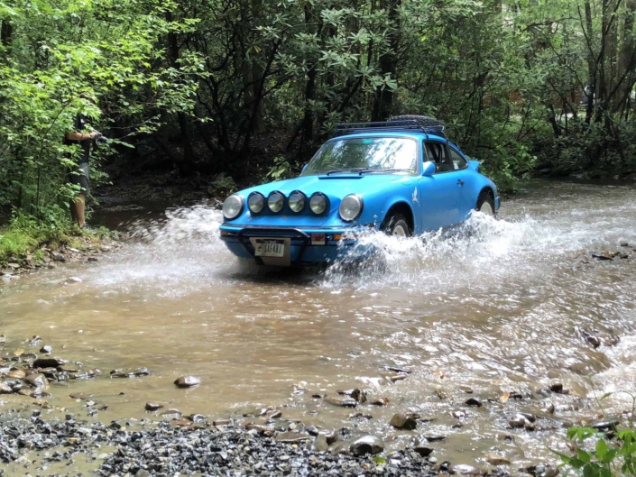 Custom Built 1980 Porsche 911 SC in Riviera Blue driving through the water in the woods