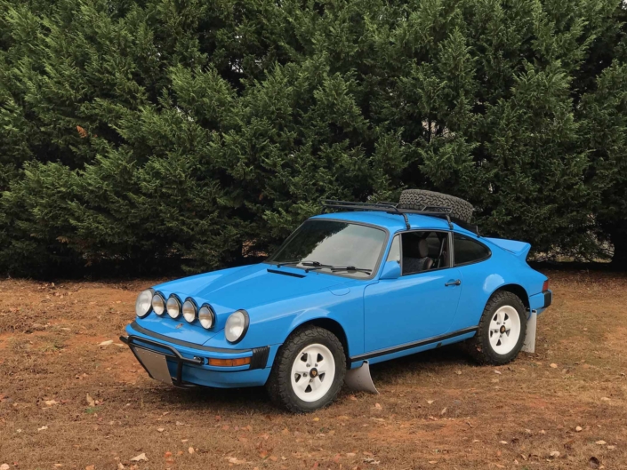 Custom Built 1980 Porsche 911 SC in Riviera Blue with blue and brown basket weave interior parked on dirt with the woods in the background