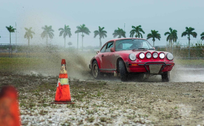 Custom Built 1981 Guards Red Porsche 911 SC spinning its wheels with palm trees in the background