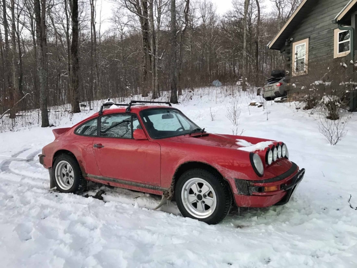 Custom Built 1981 Guards Red Porsche 911 SC parked in a snowy forest