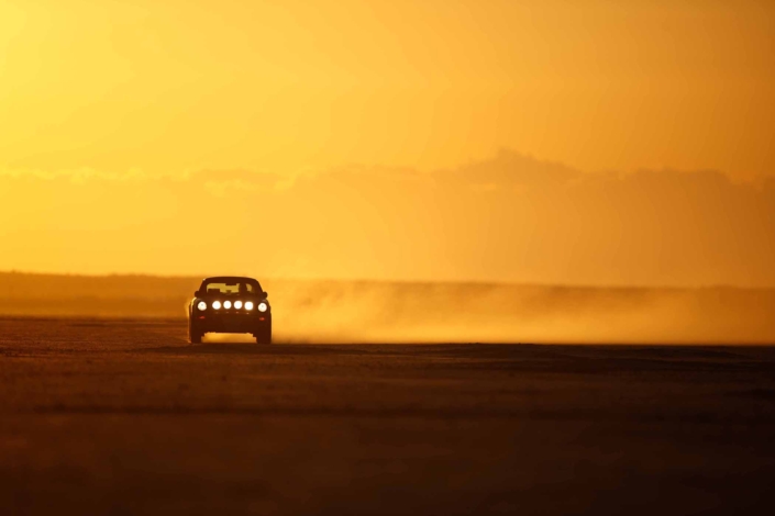 Custom Built 1987 Porsche 911 Carrera in Cassis Red with European bus fabric interior driving through the desert at sunset