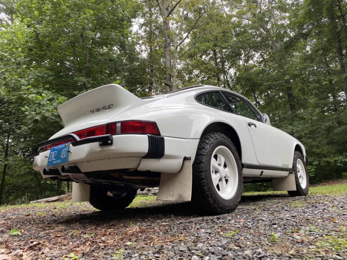 3/4 rear view of a Custom Built 1981 Porsche 911 SC with Grand Prix White exterior and Cow Interior parked in the woods