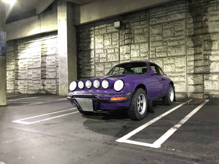Custom Built 1978 Porsche 911 SC with Lilac exterior and Pascha interior parked in a parking space with the headlights on