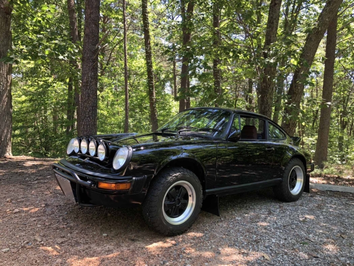 3/4 front view of Leh Keen's Custom Built 1986 Porsche 911 Carrera with Shwartz Exterior and Mercedes G Fabric Interior parked in the woods
