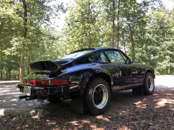 rear view of a Custom Built 1986 Porsche 911 Carrera with Shwartz Exterior and Mercedes G Fabric Interior parked in the woods