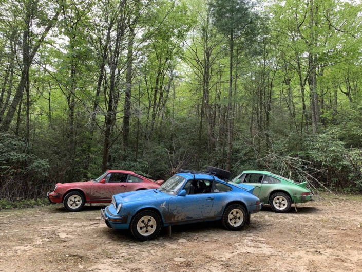 Custom Built 1980 Porsche 911 SC in Riviera Blue in front of two other custom porsches in the woods