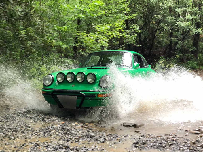 Leh Keen's Custom Built 1981 Porsche 911 SC in Signal Green with Porsche Tartan Interior driving through water in the woods