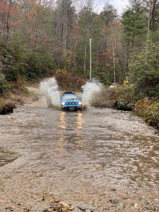 Custom Built 1980 Porsche 911 SC in Riviera Blue driving through the water in the woods