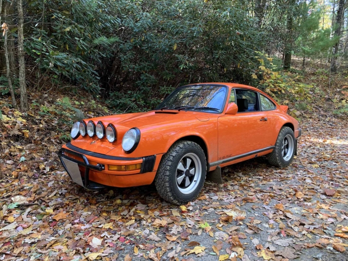 Custom built 1987 Porsche 911 Carrera with Continental Orange exterior and VW tartan interior parked in the fall folliage