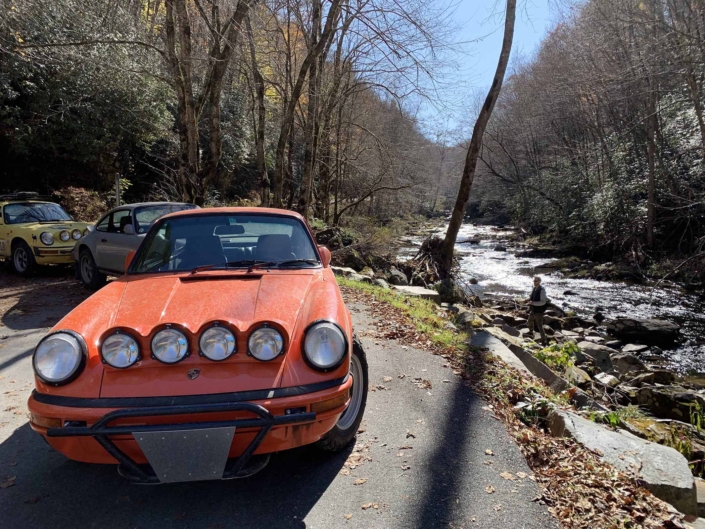 Custom built 1987 Porsche 911 Carrera with Continental Orange exterior and VW tartan interior parked in the woods