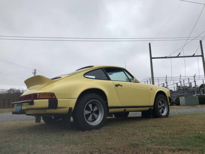 3/4 side view of a Custom Built 1984 Porsche 911 Carrera Euro with Hellgelb Exterior and Mercedes Tartan Interior on a cloudy day