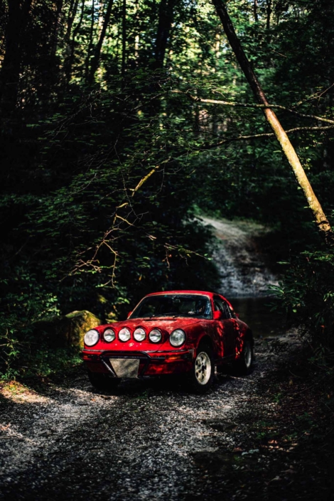 Custom Built 1981 Guards Red Porsche 911 SC driving through the woods at dusk