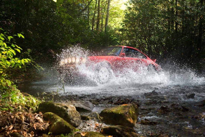 side view of the Custom Built 1981 Guards Red Porsche 911 SC driving through water in the woods