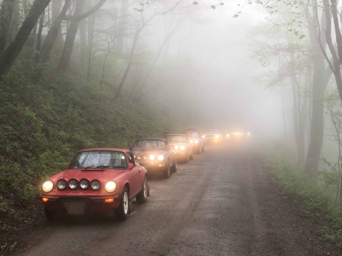 Custom Built 1981 Guards Red Porsche 911 SC parked with headlights on during a foggy day