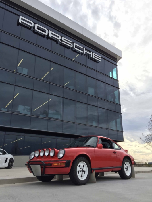 Custom Built 1981 Guards Red Porsche 911 SC parked in front of the Porsche building